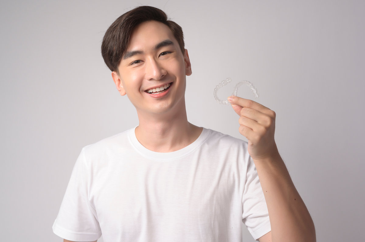 A Young smiling man holding invisalign braces over white background studio, dental healthcare and Orthodontic concept.