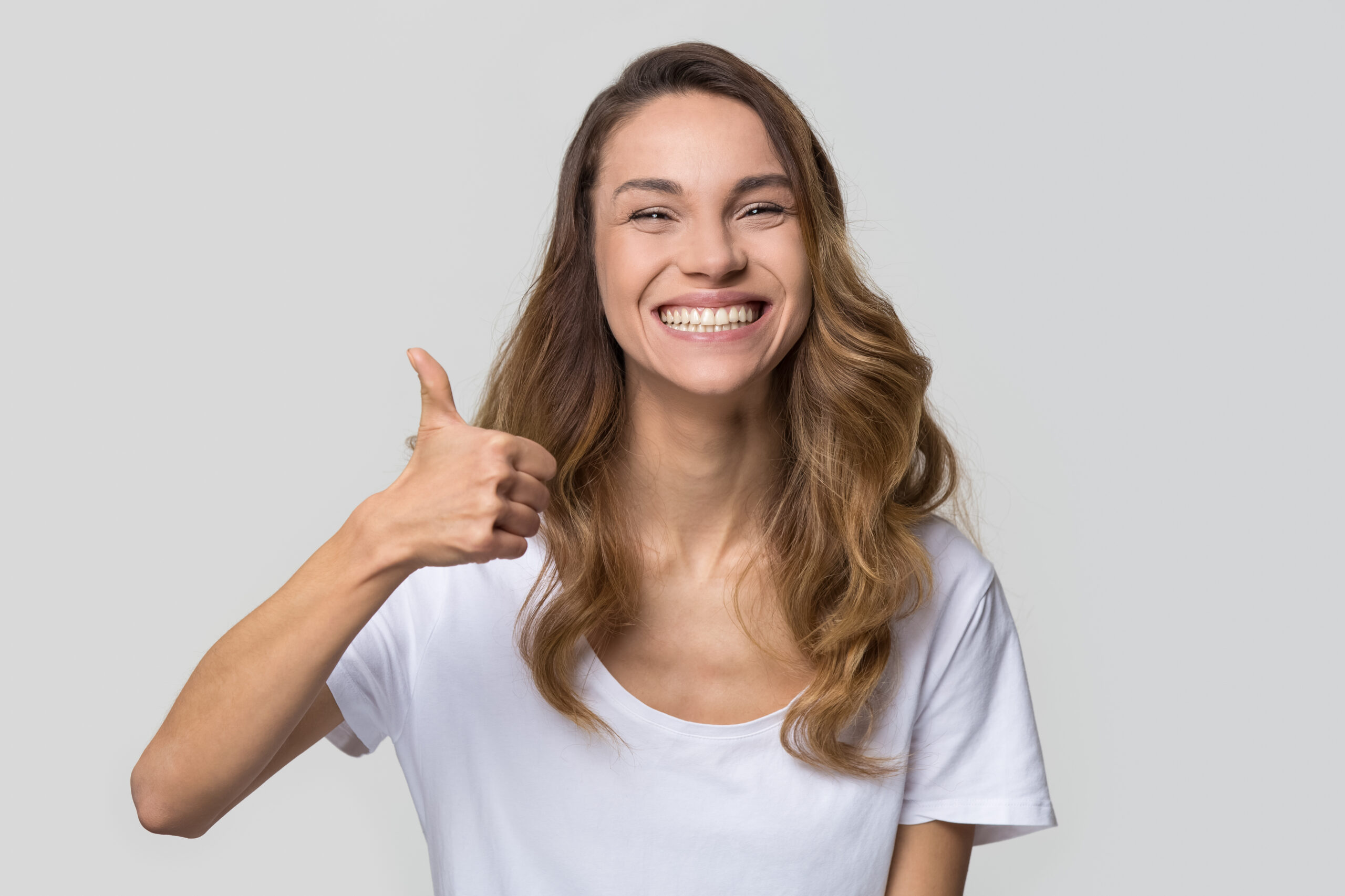 Young satisfied woman smiling with white teeth showing thumbs up looking at camera isolated on studio blank background, happy girl student like recommend dental orthodontic service concept, portrait