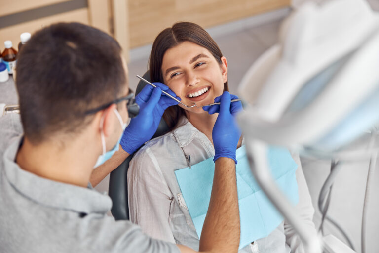 Cheerful positive dentist and client in dentistry. They look at each other and smile. Female client sit in chair.